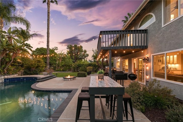 pool at dusk with a fire pit, a patio area, and an outdoor pool