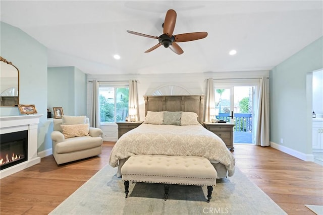 bedroom with a glass covered fireplace, access to outside, wood finished floors, baseboards, and recessed lighting