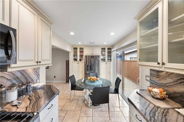 kitchen featuring stainless steel fridge, baseboards, stone tile floors, dark stone countertops, and recessed lighting