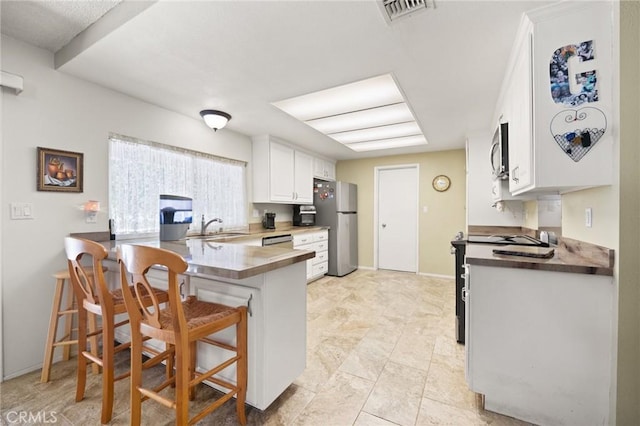54955 Benecia Trl, Yucca Valley, CA 92284 - kitchen featuring stainless steel appliances, white cabinets, a peninsula, a kitchen bar, and a sink