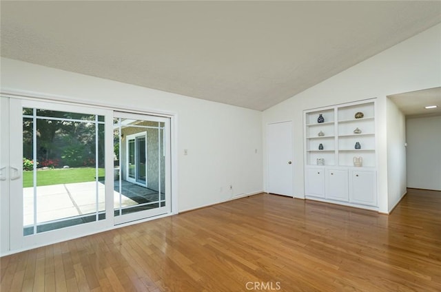 empty room with vaulted ceiling, wood-type flooring, and built in features