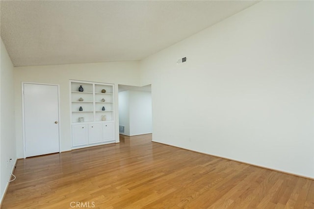 empty room featuring vaulted ceiling, light wood-type flooring, and built in features