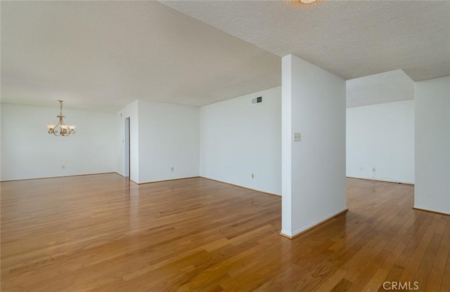 spare room with a chandelier, light wood-type flooring, and baseboards