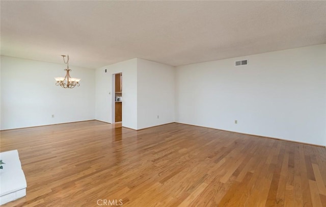 empty room featuring a chandelier and light wood-style flooring