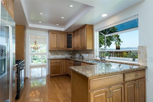 kitchen featuring stainless steel appliances, light stone counters, brown cabinetry, light wood finished floors, and tasteful backsplash