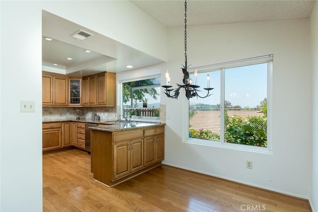 kitchen with brown cabinets, a chandelier, light wood-type flooring, glass insert cabinets, and stone counters