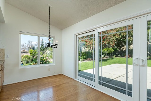 unfurnished dining area featuring hardwood / wood-style floors, vaulted ceiling, a chandelier, baseboards, and a textured ceiling