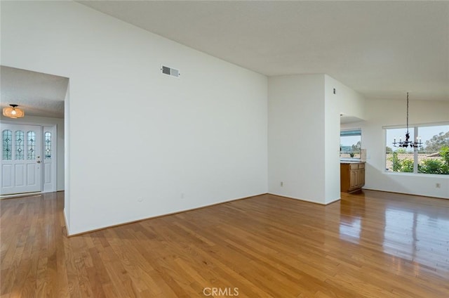 empty room with a chandelier, light wood finished floors, and lofted ceiling