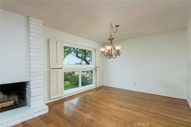 unfurnished dining area featuring wood finished floors, a textured ceiling, a chandelier, and a brick fireplace