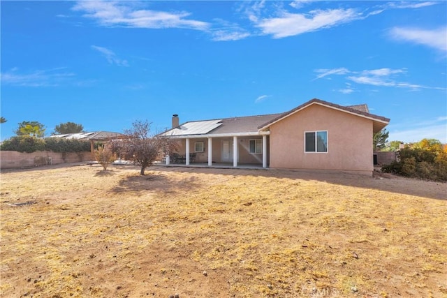 13935 Rincon Rd, Apple Valley, CA 92307 - back of house featuring roof mounted solar panels, a patio area, a chimney, stucco siding, and fence