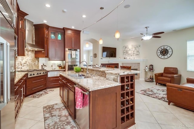 kitchen featuring open floor plan, light tile patterned floors, appliances with stainless steel finishes, wall chimney range hood, and a sink