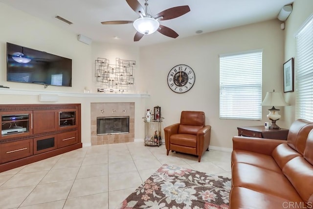 living room with a tiled fireplace, ceiling fan, light tile patterned flooring, and baseboards