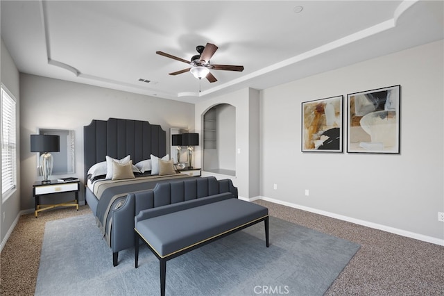 bedroom featuring carpet floors, a raised ceiling, arched walkways, and baseboards