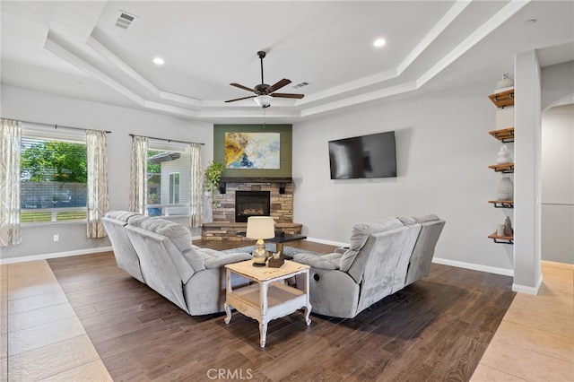 living area featuring a tray ceiling, ceiling fan, baseboards, a fireplace, and wood finished floors