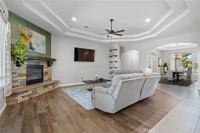living room with a raised ceiling, arched walkways, a stone fireplace, wood finished floors, and recessed lighting