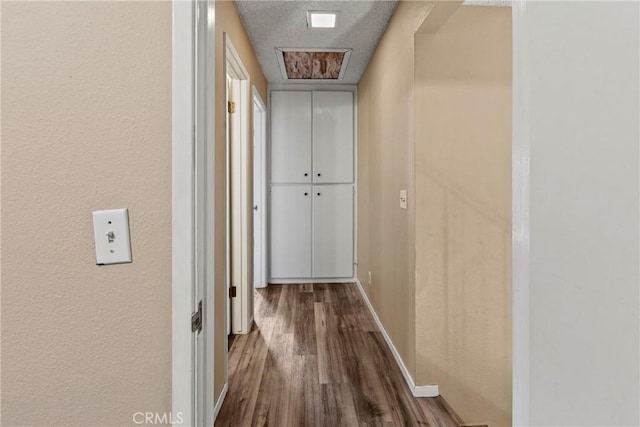 hall with wood finished floors, a textured wall, and baseboards