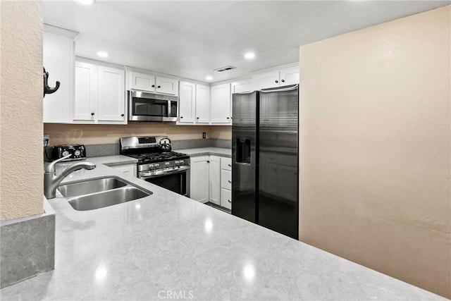 kitchen featuring appliances with stainless steel finishes, a sink, recessed lighting, white cabinets, and light stone countertops