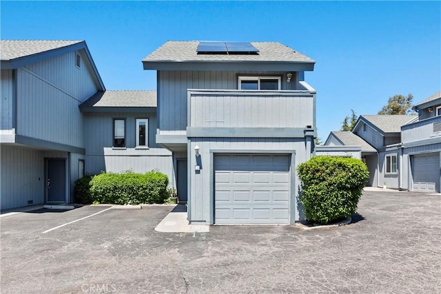 multi unit property with solar panels, roof with shingles, and a balcony