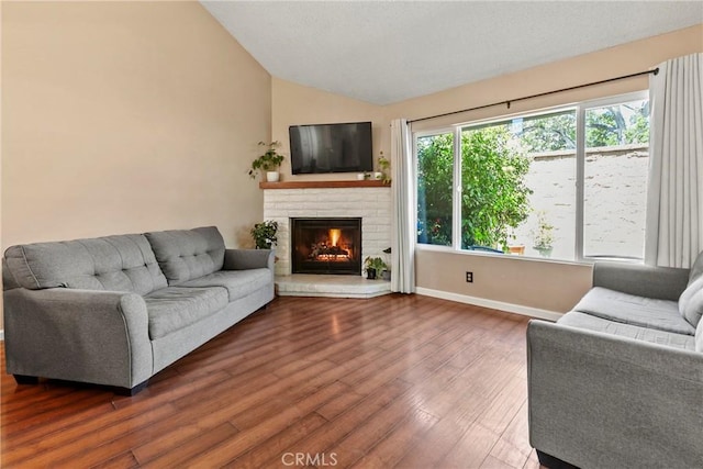 living room featuring vaulted ceiling, a brick fireplace, dark wood-style floors, and baseboards