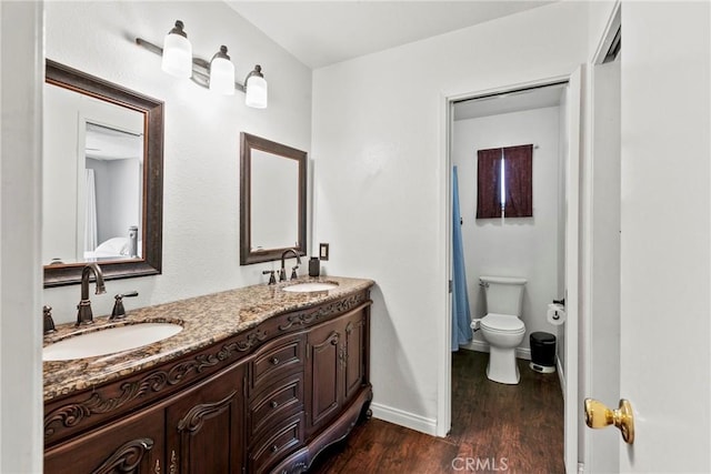 bathroom featuring wood finished floors, toilet, baseboards, and double vanity