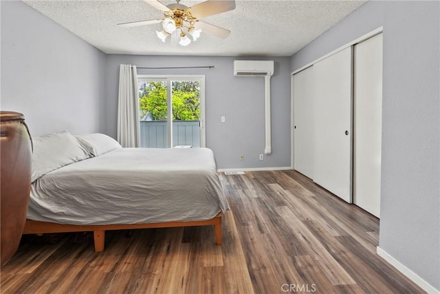 bedroom with a wall unit AC, access to exterior, a textured ceiling, wood finished floors, and baseboards