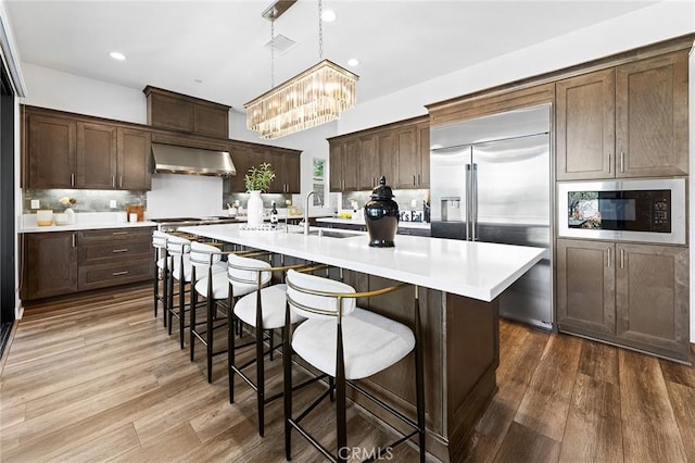 27 Alessio, Lake Forest, CA 92630 - kitchen featuring wall chimney exhaust hood, built in appliances, backsplash, dark wood finished floors, and recessed lighting