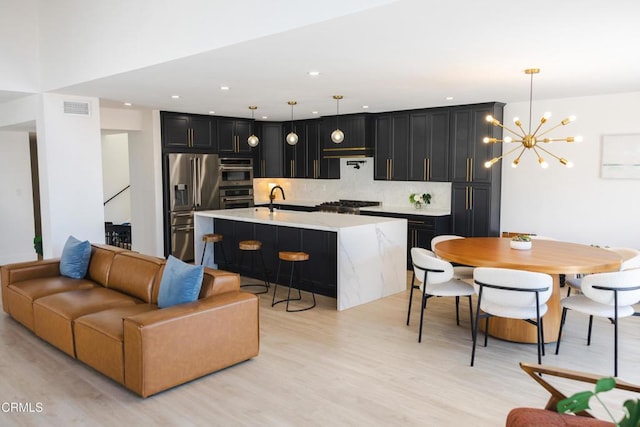 3960 W Hemlock St, Oxnard, CA 93035 - kitchen with stainless steel appliances, dark cabinetry, backsplash, light wood-type flooring, and a chandelier