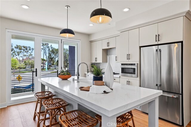 19041 Main St Unit 109, Huntington Beach, CA 92648 - kitchen with appliances with stainless steel finishes, a kitchen bar, light wood finished floors, white cabinets, and decorative light fixtures