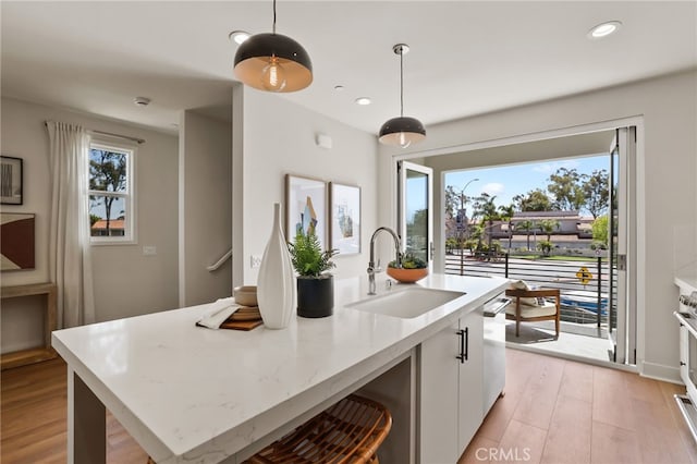19041 Main St Unit 109, Huntington Beach, CA 92648 - kitchen featuring a sink, a kitchen island with sink, hanging light fixtures, light wood-type flooring, and white cabinets