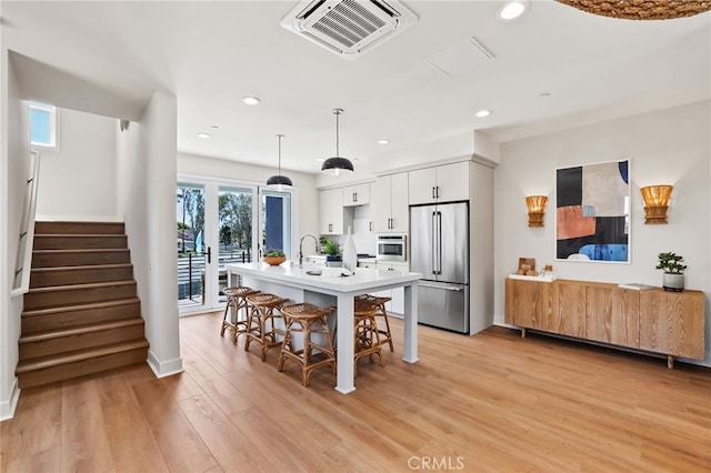 19041 Main St Unit 109, Huntington Beach, CA 92648 - kitchen with high end refrigerator, a kitchen breakfast bar, light wood-style floors, white cabinetry, and a center island with sink