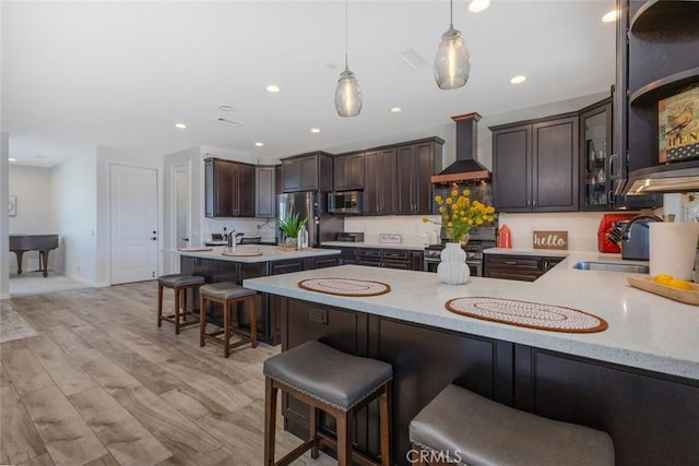 38550 Crossover Rd, Temecula, CA 92592 - kitchen with stainless steel appliances, wall chimney exhaust hood, dark brown cabinetry, a kitchen bar, and recessed lighting