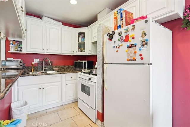 kitchen with white appliances, a sink, white cabinets, light tile patterned floors, and dark stone countertops