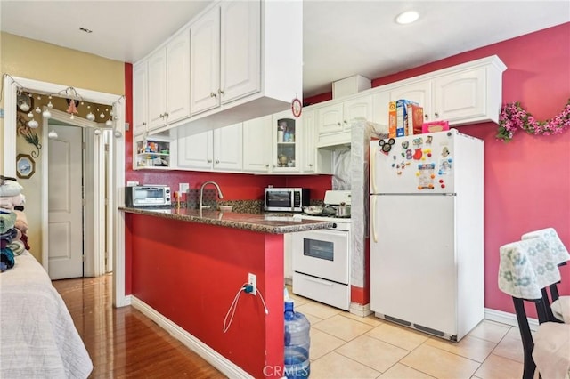 kitchen with white appliances, white cabinets, dark countertops, glass insert cabinets, and a sink