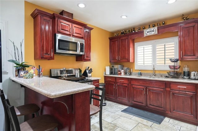 kitchen with stainless steel microwave, a sink, reddish brown cabinets, and recessed lighting