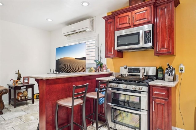 kitchen with stainless steel appliances, dark brown cabinets, an AC wall unit, a breakfast bar area, and light countertops