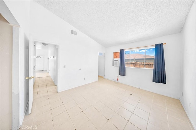 spare room with a textured ceiling, vaulted ceiling, and light tile patterned floors