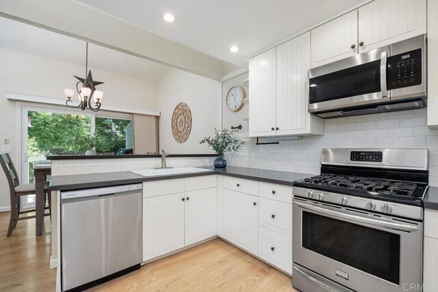 1715 Kennington Rd, Encinitas, CA 92024 - kitchen featuring stainless steel appliances, a sink, a peninsula, dark countertops, and a chandelier