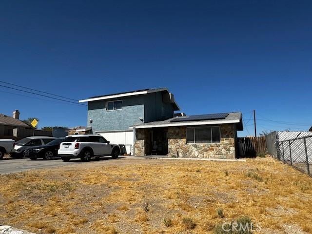 view of front facade featuring roof mounted solar panels, stone siding, fence, concrete driveway, and an attached garage