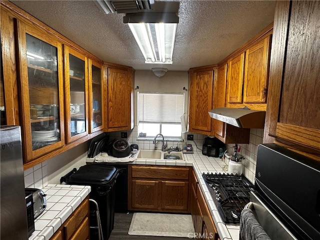 351 Armory Rd, Barstow, CA 92311 - kitchen featuring a sink, tile counters, brown cabinetry, a textured ceiling, and glass insert cabinets