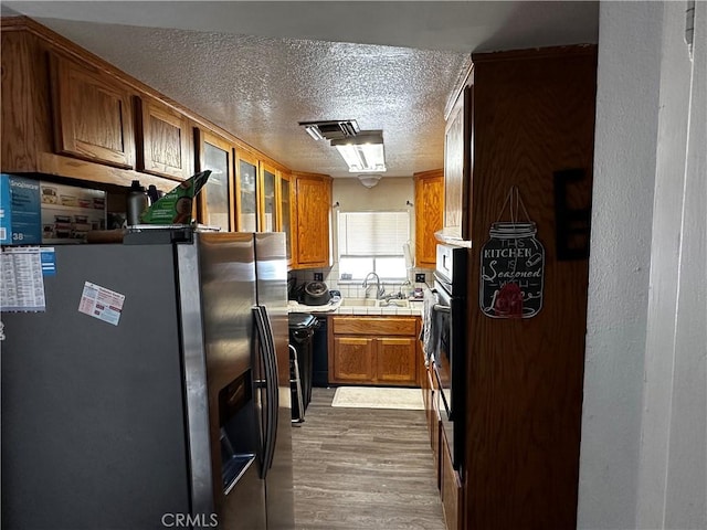 351 Armory Rd, Barstow, CA 92311 - kitchen featuring stainless steel fridge, a textured ceiling, dark wood-style floors, brown cabinetry, and glass insert cabinets