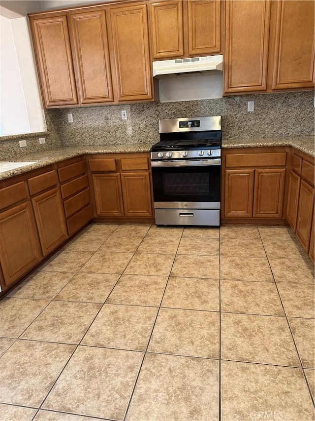 11946 Russell Ct, Victorville, CA 92392 - kitchen with stainless steel gas range, under cabinet range hood, decorative backsplash, brown cabinets, and light stone countertops
