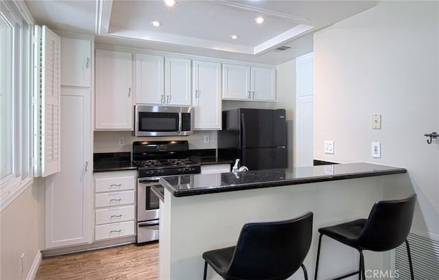 28071 Caldaro, Laguna Niguel, CA 92677 - kitchen with appliances with stainless steel finishes, a tray ceiling, a peninsula, a breakfast bar, and white cabinetry
