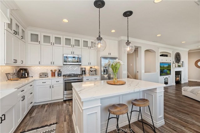 1663 Spyglass Dr, Corona, CA 92883 - kitchen with stainless steel appliances, open floor plan, a kitchen bar, white cabinets, and crown molding