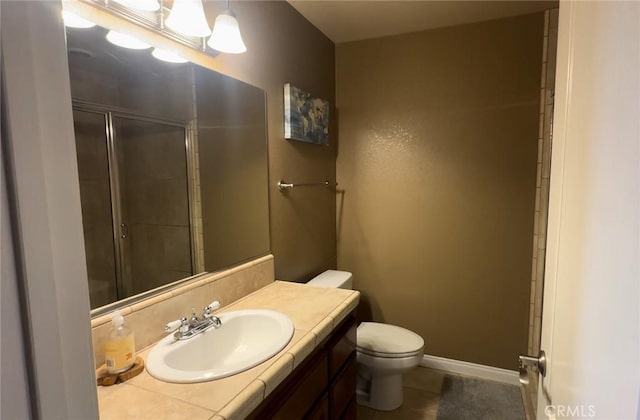 bathroom with toilet, a shower with shower door, vanity, tile patterned floors, and baseboards