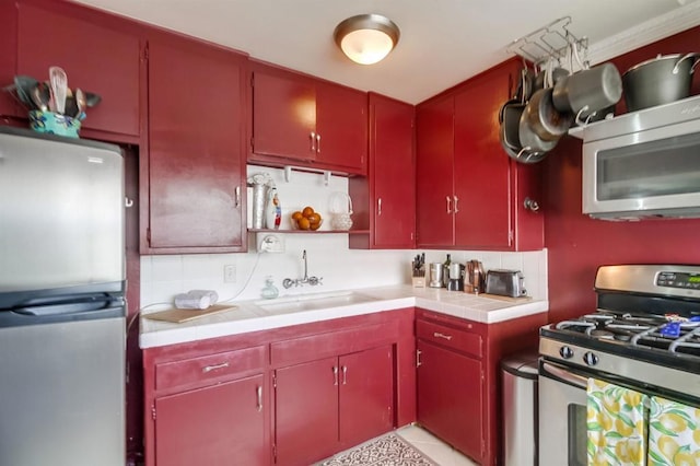kitchen with appliances with stainless steel finishes, red cabinetry, a sink, and backsplash