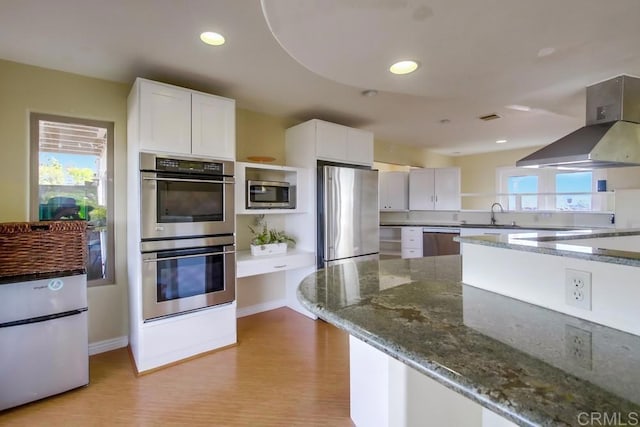 2638 W Victoria Dr, Alpine, CA 91901 - kitchen featuring appliances with stainless steel finishes, wall chimney exhaust hood, dark stone counters, light wood finished floors, and white cabinets