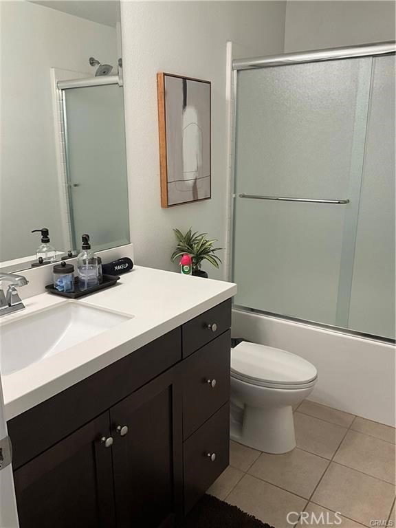 full bathroom featuring vanity, toilet, tile patterned floors, and bath / shower combo with glass door