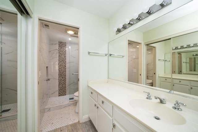 bathroom with toilet, a marble finish shower, wood finished floors, and vanity