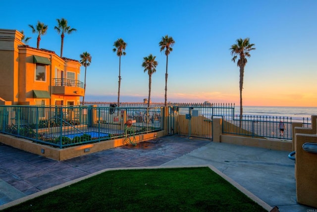 patio terrace at dusk with a gate, a water view, fence, and a balcony