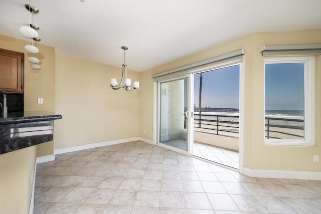 unfurnished dining area with a chandelier, baseboards, and a water view